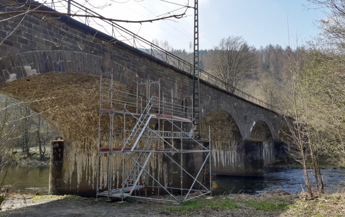 Eine Eisenbahnbrücke aus Stein. An der Brücke steht ein Gerüst für Arbeiter. An dieser Brücke hat die EPV-GIV Vermessungsarbeiten vorgenommen.